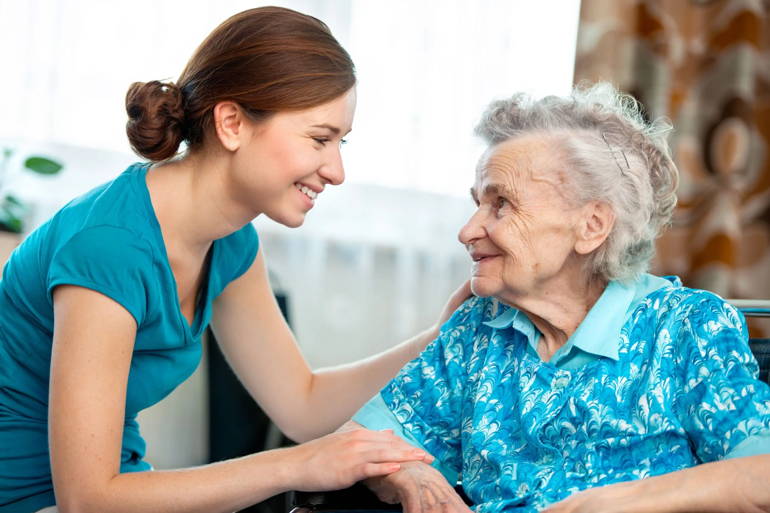 A caregiver smiles warmly at an elderly woman in a wheelchair, fostering a compassionate connection in a bright, welcoming environment.