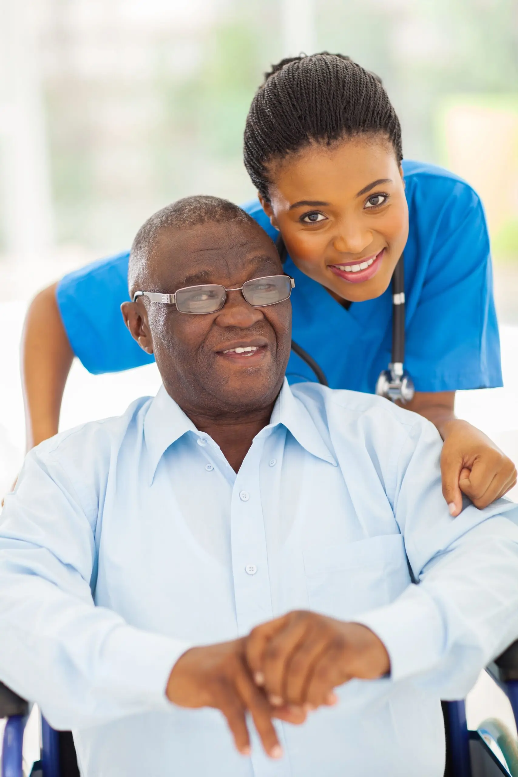 A caregiver smiles alongside an elderly patient in a wheelchair, showcasing compassionate healthcare support in a bright, nurturing environment.