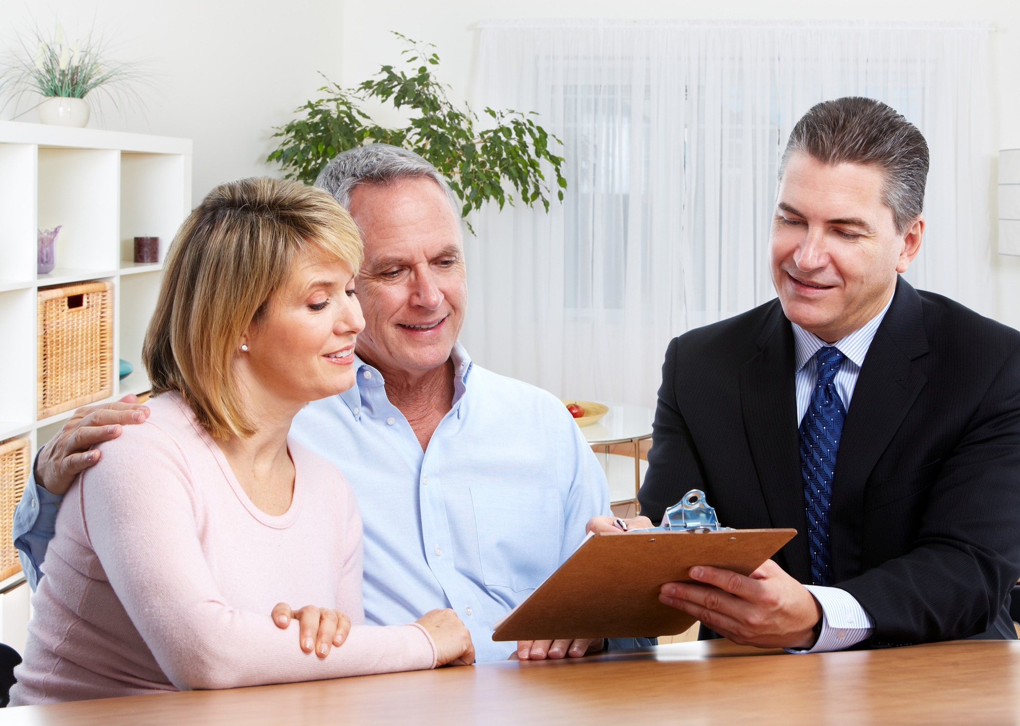 A couple discusses plans with a financial advisor in a bright office setting, focused on paperwork, symbolizing financial guidance and partnership.